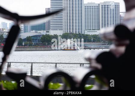 Durch die Skulpturenöffnung sehen Sie den berühmten Merlion von Singapur, den Bumboat-Service für Touristen und das 5-Sterne-Hotel im Hintergrund. Stockfoto