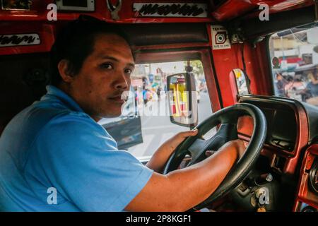 Mark, ein Jeepney-Fahrer, fährt einen traditionellen Jeepney, um Passagiere zu befördern. Seit Jahrzehnten verlassen sich Pendler auf Jeepneys, eine lebendige und ikonische Transportmethode auf den Philippinen. Es gilt als eine ikonische Darstellung des philippinischen Transports und hat sich zu einem nationalen Symbol entwickelt. Die ersten Jeepneys wurden aus amerikanischen Militärjeeps, die nach dem Zweiten Weltkrieg auf den Philippinen verlassen worden waren, in einzigartige Fahrzeuge für den öffentlichen Nahverkehr umgewandelt, die bis zu 20 Passagiere aufnehmen konnten. In zehn Jahren drängt die Regierung auf eine Modernisierungsinitiative, um veraltete je zu ersetzen Stockfoto