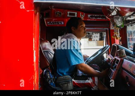 Mark, ein Jeepney-Fahrer, fährt einen traditionellen Jeepney zum Transit. Seit Jahrzehnten verlassen sich Pendler auf Jeepneys, eine lebendige und ikonische Transportmethode auf den Philippinen. Es gilt als eine ikonische Darstellung des philippinischen Transports und hat sich zu einem nationalen Symbol entwickelt. Die ersten Jeepneys wurden aus amerikanischen Militärjeeps, die nach dem Zweiten Weltkrieg auf den Philippinen verlassen worden waren, in einzigartige Fahrzeuge für den öffentlichen Nahverkehr umgewandelt, die bis zu 20 Passagiere aufnehmen konnten. In zehn Jahren drängt die Regierung auf eine Modernisierungsinitiative, um veraltete Jeepneys durch zu ersetzen Stockfoto