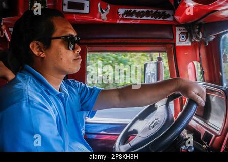 Mark, ein Jeepney-Fahrer, fährt einen traditionellen Jeepney, um Passagiere zu befördern. Seit Jahrzehnten verlassen sich Pendler auf Jeepneys, eine lebendige und ikonische Transportmethode auf den Philippinen. Es gilt als eine ikonische Darstellung des philippinischen Transports und hat sich zu einem nationalen Symbol entwickelt. Die ersten Jeepneys wurden aus amerikanischen Militärjeeps, die nach dem Zweiten Weltkrieg auf den Philippinen verlassen worden waren, in einzigartige Fahrzeuge für den öffentlichen Nahverkehr umgewandelt, die bis zu 20 Passagiere aufnehmen konnten. In zehn Jahren drängt die Regierung auf eine Modernisierungsinitiative, um veraltete je zu ersetzen Stockfoto