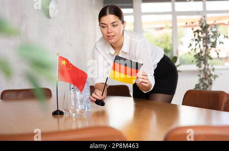 Vorbereitung auf Geschäftsverhandlungen - Frau setzt kleine Flaggen von Ländern Chinas und Deutschlands auf den Tisch Stockfoto