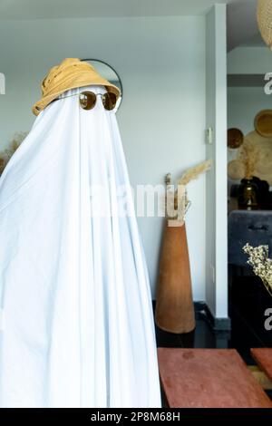 Eine Person mit Hut und schwarzer Sonnenbrille über einem weißen Tuch, das einem Geist ähnelt Stockfoto