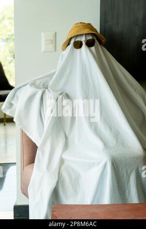 Eine Person mit Hut und schwarzer Sonnenbrille über einem weißen Tuch, das einem Geist ähnelt Stockfoto