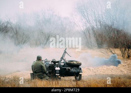 Re-enactor gekleidet als Wehrmachts-Infanterie-Soldat der Zweiten Weltkrieg sitzen in der Nähe von Old Tricar, bewaffneter Maschinengewehr. Rauchwand. Armee Dreirad Motorrad Stockfoto