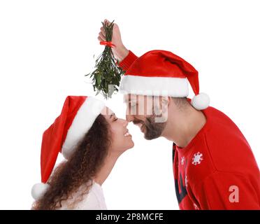 Ein hübsches Paar in Weihnachtsmannhüten unter Mistelzweigen auf weißem Hintergrund Stockfoto