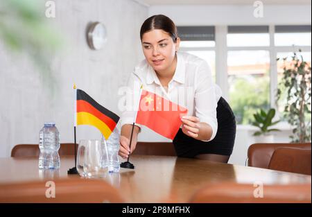 Vorbereitung auf Geschäftsverhandlungen - Frau setzt kleine Flaggen von Ländern Chinas und Deutschlands auf den Tisch Stockfoto