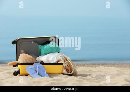 Offener Koffer mit Strandgegenständen am Sandstrand, Platz für Text Stockfoto