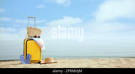 Gelber Koffer mit Strandgegenständen am Sandstrand, Platz für Text Stockfoto