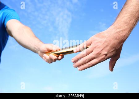 Ein Mann, der seinen Stab an seinen Partner weitergibt, gegen den blauen Himmel, Nahaufnahme Stockfoto