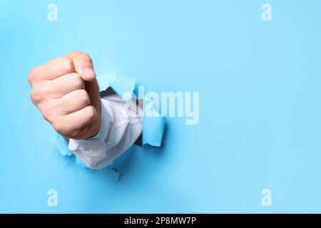 Ein Geschäftsmann, der mit der Faust durch hellblaues Papier bricht, eine Nahaufnahme. Platz für Text Stockfoto