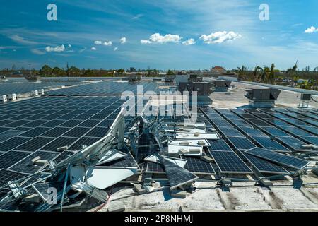 Draufsicht der durch den Hurrikan Ian zerstörten Photovoltaik-Solarpaneele, die auf dem Dach des Industriebaues zur Erzeugung von ökologischem Strom montiert sind. Konse Stockfoto