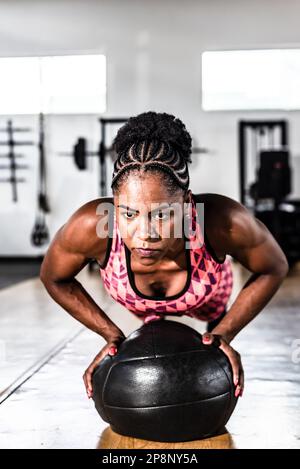 Entschlossene Frau, die mit einem Ball im Fitnessstudio Unterstützung leistet. Wirbelsäule und Arme stärken. Stockfoto
