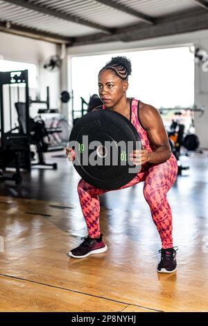 Fitness-Frau, die Kniebeugen mit der Barglocke im Crossfit-Gym macht. Gesundheitskonzept. Stockfoto