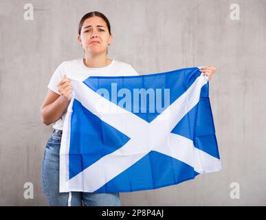 Verärgerte junge Frau mit schottischer Flagge. Isoliert auf grauem Hintergrund Stockfoto