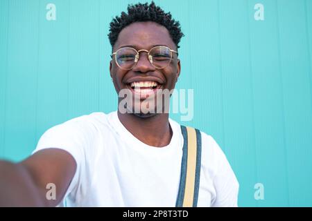 Selfie eines fröhlichen gutaussehenden Mannes auf der Straße. Portarit eines glücklichen jungen Mannes, der ein Selfie-Foto auf der Kamera macht, auf einer türkisfarbenen Hintergrundwand. Stockfoto