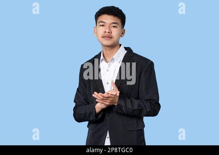 Junger, gutaussehender asiatischer Geschäftsmann, der stolz lächelt und isoliert auf blauem Hintergrund klatscht Stockfoto