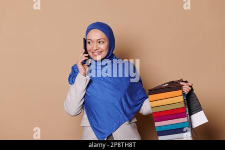 Charmante muslimische Frau in Hidschab, Verkaufsleiter, Dekorateur spricht am Handy, nimmt Bestellungen für Sofabezüge entgegen Stockfoto