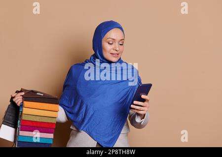 Eine selbstbewusste muslimische Frau in Hijab, Innenarchitekt, der das Telefon benutzt, nimmt Bestellungen für Polstermaterialien über mobile Apps entgegen Stockfoto