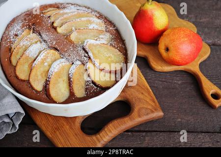 Schokoladenbrownie mit einer Birne in einer Backform. Essen sammeln Stil. Herbsthintergrund. Zutaten für die Zubereitung Stockfoto