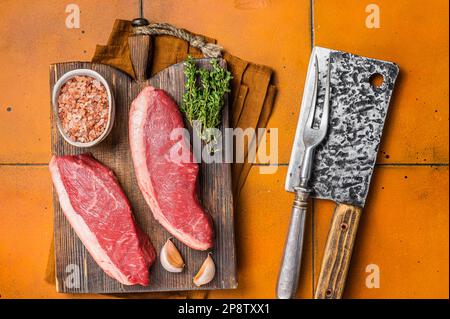 Cap Rump Steak, rohes Rindfleisch Steak mit Thymian und Salz auf Holzbrettern. Orangefarbener Hintergrund. Draufsicht. Stockfoto