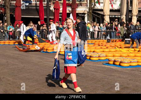 Das Käsemädchen in traditionellem Kostüm und Holzschuhen geht mit ihren Waren lächelnd durch den Käsemarkt in der Stadt Alkmaar. Stockfoto