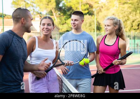 Zwei Tennisspielerpaare diskutieren gern über ein vergangenes Spiel auf einem offenen Platz Stockfoto