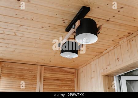 Innenausstattung, Decke. Stilvolle skandinavische Zusammensetzung aus schwarzem BH und Holzwänden. Loft-Stil mit moderner Inneneinrichtung. Stockfoto