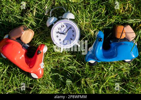 Spielzeugroller und Wecker auf grünem Gras. Lieferung, Reisekonzept. Stockfoto