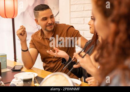 Entspannte Freunde treffen sich mit jungen Männern und zwei Frauen, plaudern im Restaurant, gesellige Lebensweise, kleine Gruppe von Leuten Stockfoto