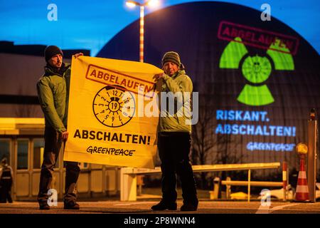 09. März 2023, Baden-Württemberg, Neckarwestheim: Greenpeace-Aktivisten protestieren gegen die Kernkraft vor dem Kernkraftwerk Neckarwestheim. Sie halten ein Poster mit einem abgelaufenen HU-Aufkleber und den Worten „abgelaufen“ und „Schluss! Gleichzeitig wird das gleiche mit Hilfe eines großen Projektors auf das Kernkraftwerk projiziert. Greenpeace macht mit seinem Handeln darauf aufmerksam, dass die drei Kernkraftwerke Lingen, Isar 2 und Neckarwestheim 2019 einer Sicherheitsüberprüfung unterzogen worden wären, die laut Greenpeace noch nicht durchgeführt worden sei. Foto: Chris Stockfoto