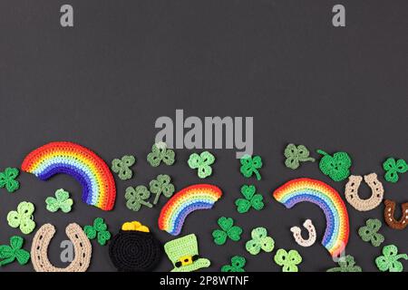 St. Patrick's Day Konzept. Gestrickte Komposition aus grünem Hut, goldenem Topf, Hufeisen, Regenbogen und grünen Shamrocks auf schwarzem Hintergrund Stockfoto