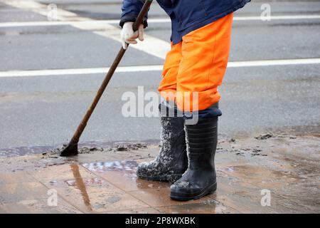 Der Arbeiter bricht Eis und schmilzt Schnee auf der Straße mit einem Brecheisen. Schneeräumung in der Stadt, Straßenreinigung im Frühling Stockfoto