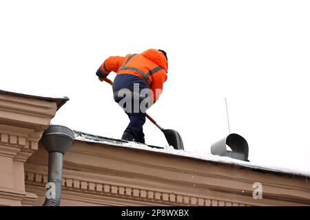 Arbeiter, der Schnee auf dem Dach eines Gebäudes entfernt. Schneeräumung, Dachreinigung im Winter oder Frühling Stockfoto