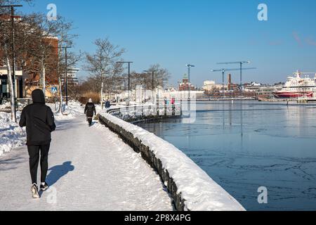 Menschen, die an einem sonnigen Wintertag in Helsinki, Finnland, auf der Promenade von Kaivopuisto joggen und spazieren gehen Stockfoto