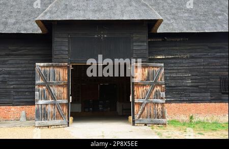 Alte strohgedeckte Scheune mit großen offenen Türen. Stockfoto