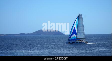 PLAYA BLANCA, LANZAROTE, SPANIEN - 29. MÄRZ 2022: Yacht mit der Nordküste von Fuerteventura und der Insel Lobos im Hintergrund. Stockfoto