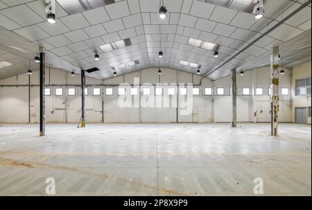 Geräumiges großes Zimmer für ein Lagerhaus oder einen Parkplatz mit Fenstern mit Metallsäulen und einer Decke, die für kosmetische Reparaturen vorbereitet ist. Das Konzept des Geschäfts Stockfoto