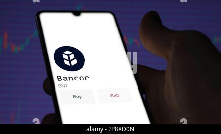 Ein Investor analysiert die Bancor ( )-Münze auf der Leinwand. Ein Telefon zeigt die Preise der Kryptos für die Investition in Ampere-Token an. Stockfoto