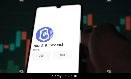 Ein Investor analysiert das Band-Protokoll ( ) auf dem Bildschirm. Ein Telefon zeigt die Preise der Kryptos für die Investition in Ampere-Token an. Stockfoto