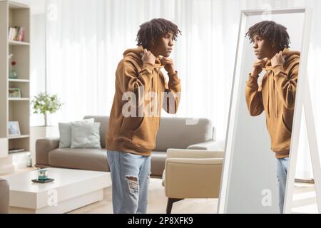Ein junger afroamerikanischer Mann, der zu Hause vor einem Spiegel steht Stockfoto