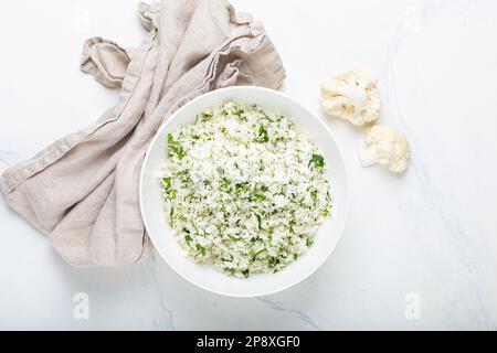 Roher Blumenkohl-Reis oder Couscous mit Dill in weißer Schüssel, gesunde kohlenhydratarme Gemüse-Beilage für Keto-Diät und gesunde kalorienarme Ernährung Stockfoto