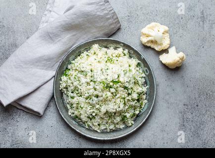 Roher Blumenkohl-Reis oder Couscous mit Dill in einer weißen Schüssel, gesunde kohlenhydratarme Gemüse-Beilage für Keto-Diät und gesunde kalorienarme Ernährung Stockfoto