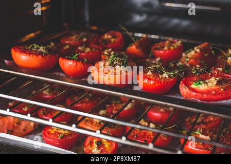 Halbierte Tomaten mit Kräutern und Knoblauch auf Backblech vorbereiten Im Ofen zum Konservieren Stockfoto