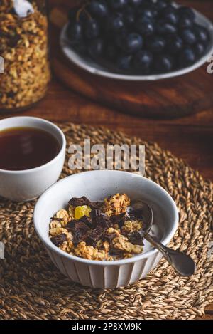 Müsli mit getrockneten Früchten und Schokolade in einer Schüssel und einer Tasse schwarzem Kaffee Stockfoto