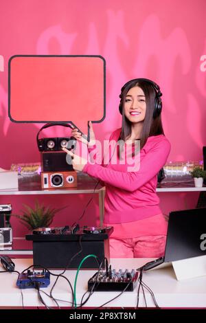 Asiatischer Künstler mit roter Sprechblase, der Textnachrichten aus Pappe im Studio auf pinkfarbenem Hintergrund präsentiert. Ein Musiker, der Musik auf einer professionellen Mixerkonsole erzeugt Stockfoto