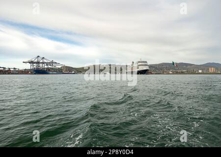 Ensenada, Baja California, Mexiko - Blick vom Ozean des Hafens mit angedocktem Frachtschiff und Kreuzfahrtschiff Stockfoto