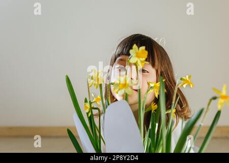 Porträt eines kleinen Mädchens, das sich hinter gelben Narzissen in einem Topf mit osterhäschen-Ohren versteckt Stockfoto