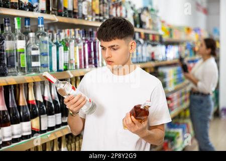 Der Mann hat im Supermarkt die Wahl zwischen Wodka und Cognac Stockfoto