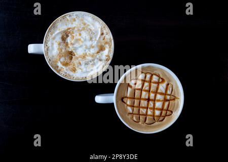 Zwei weiße Tassen mit Latte-Getränken in weißen Tassen auf einem dunklen Tisch, Draufsicht Stockfoto