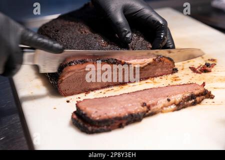 Rinderbrust wird mit einem Messer auf einem weißen Schneidebrett in Streifen geschnitten Stockfoto